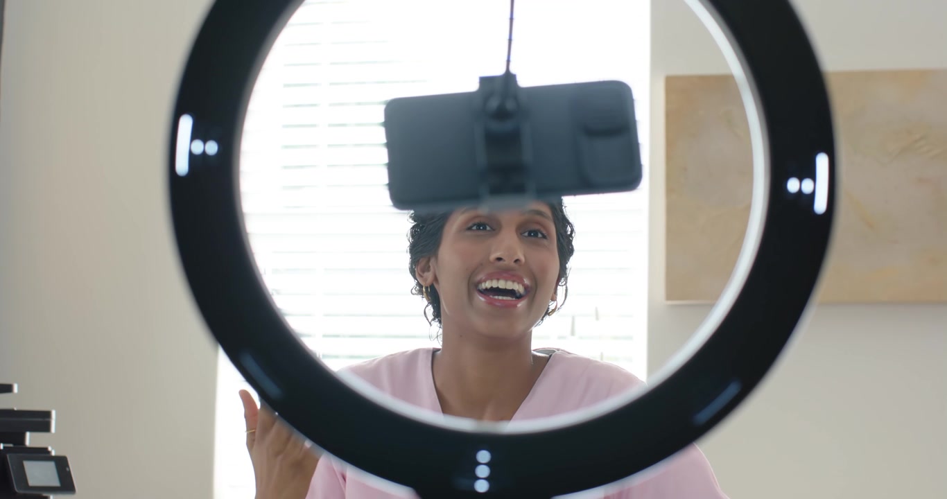 Donna afroamericana che inizia a registrare dietro un ring light, parlando nello smartphone e gesticolando