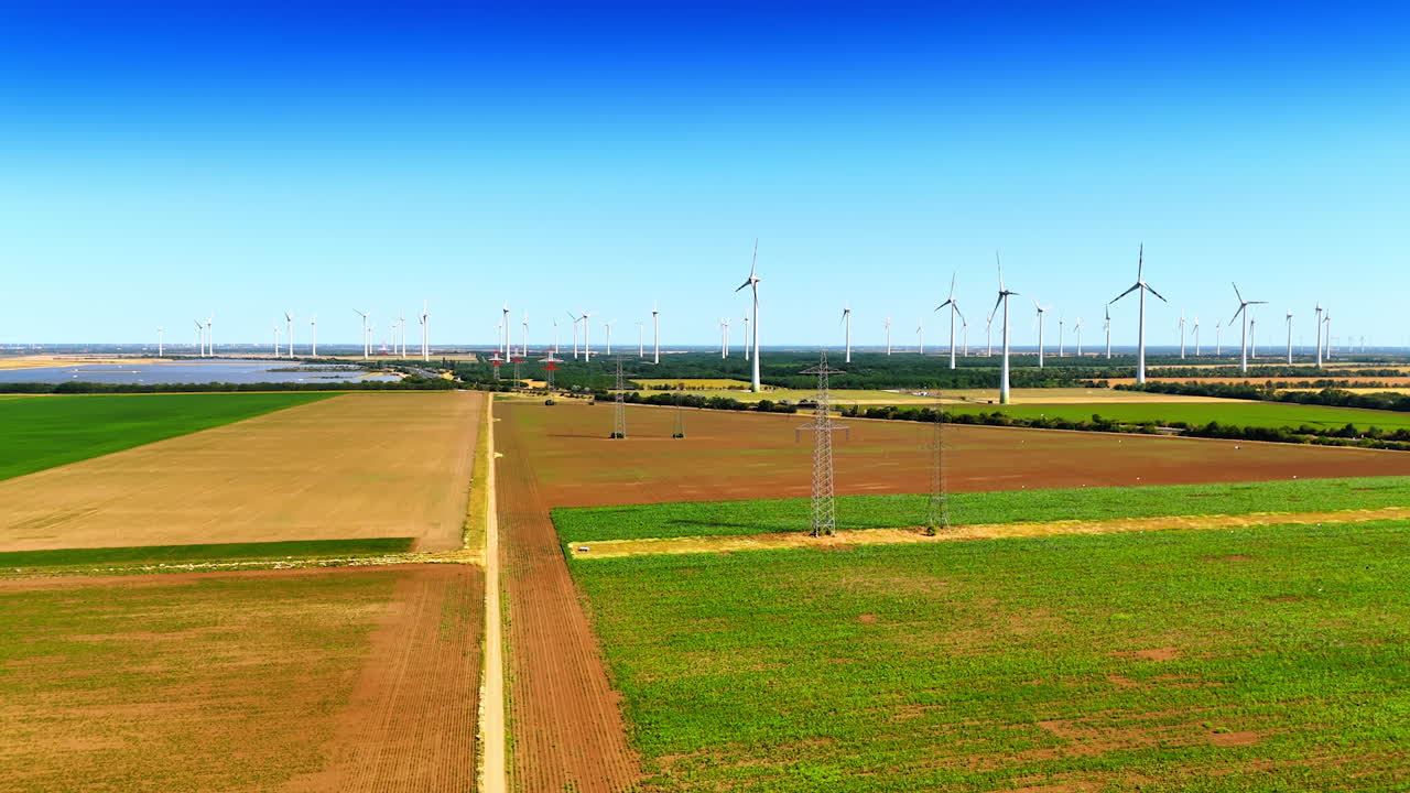 Rising over the path in the agricultural field on sunny day. Revealing view on the wind mills and electric power lines in the countryside