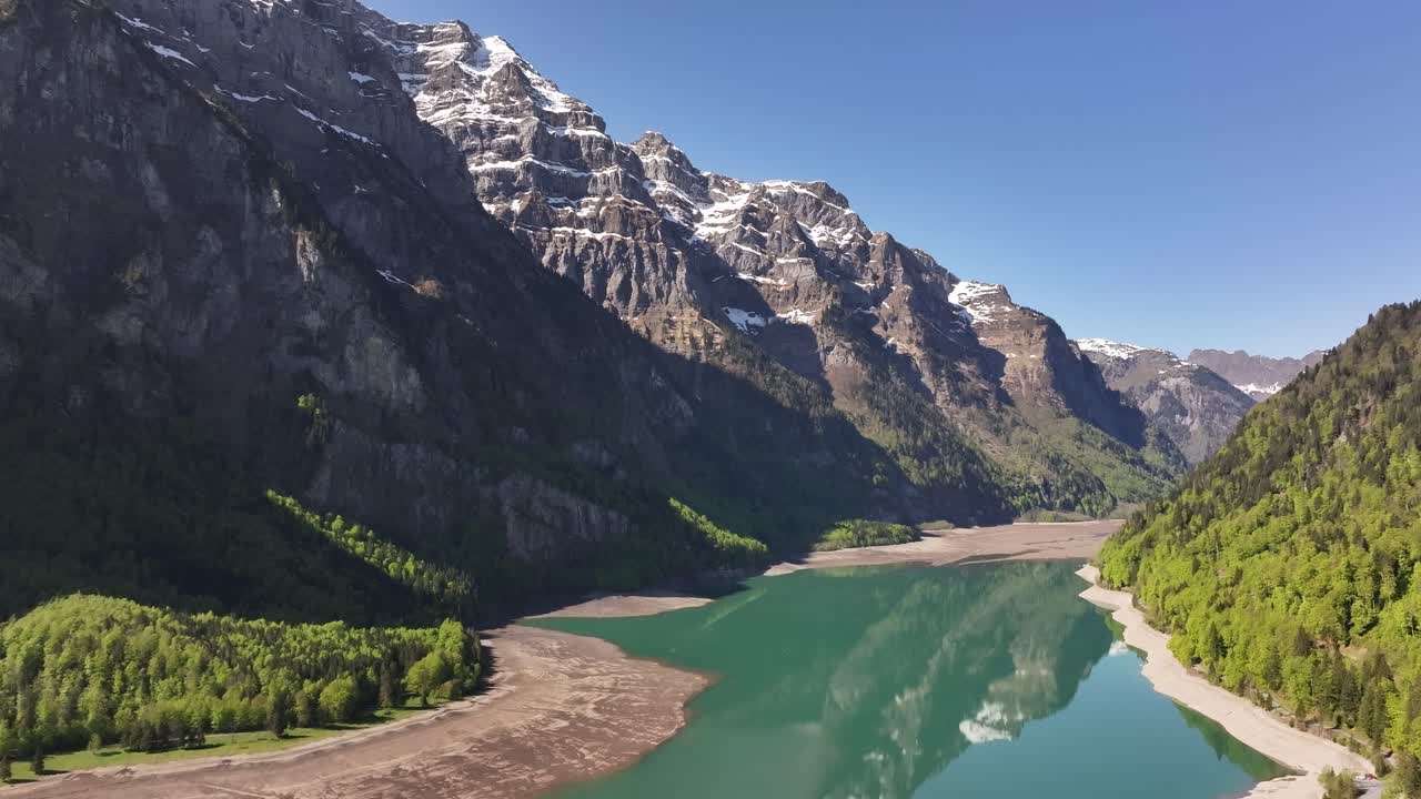 Klöntalersee in Glarus, Switzerland beautiful drone pull-back view, clear turquoise lake, snowy alps and forest reflection under blue sky