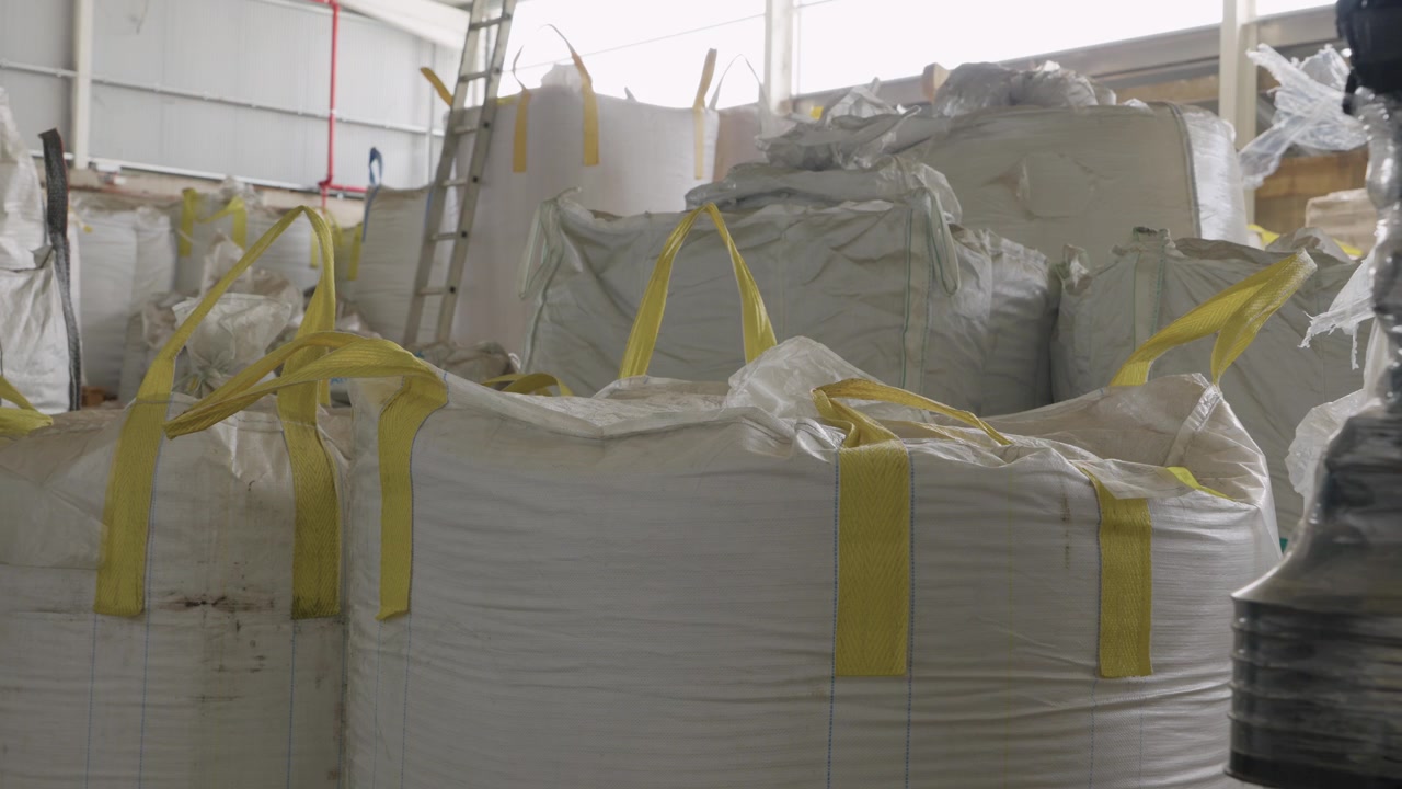 Rows of large white bulk bags with yellow straps filled with plastic waste in recycling warehouse