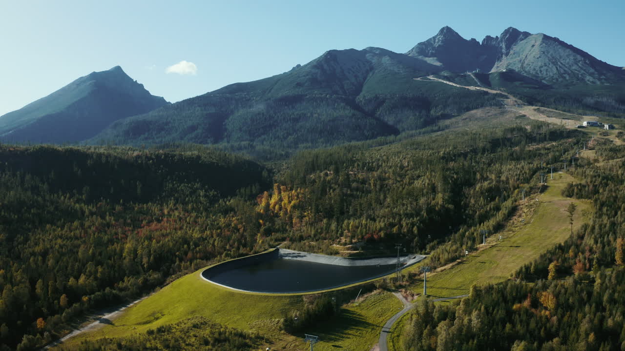 fotografía aérea de un avión no tripulado navegando de derecha a izquierda alrededor de la presa de agua en los altos tatras, mostrando árboles verdes de verano, colinas y montañas en eslovaquia, europa