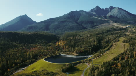 aerial drone shot cruising from right to left around the water dam in the high tatras, showcasing green summer trees, hills, and mountains in slovakia, europe
