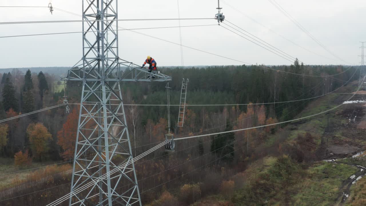 Wide shot of repair man on pylon and electrical power lines in forest surroundings
