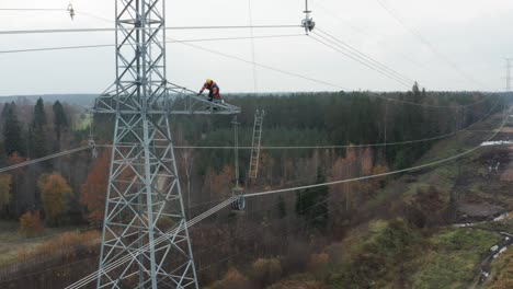 Wide-shot-of-repair-man-on-pylon-and-electrical-power-lines-in-forest-surroundings