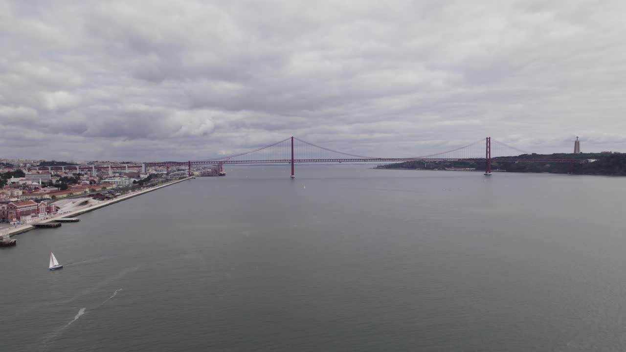 Avvicinamento aereo al ponte 25 de Abril e alla statua del Cristo Re in una giornata nuvolosa
