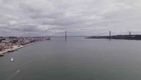 aerial hacia adelante al puente ponte 25 de abril y la estatua de cristo rey en un día nublado
