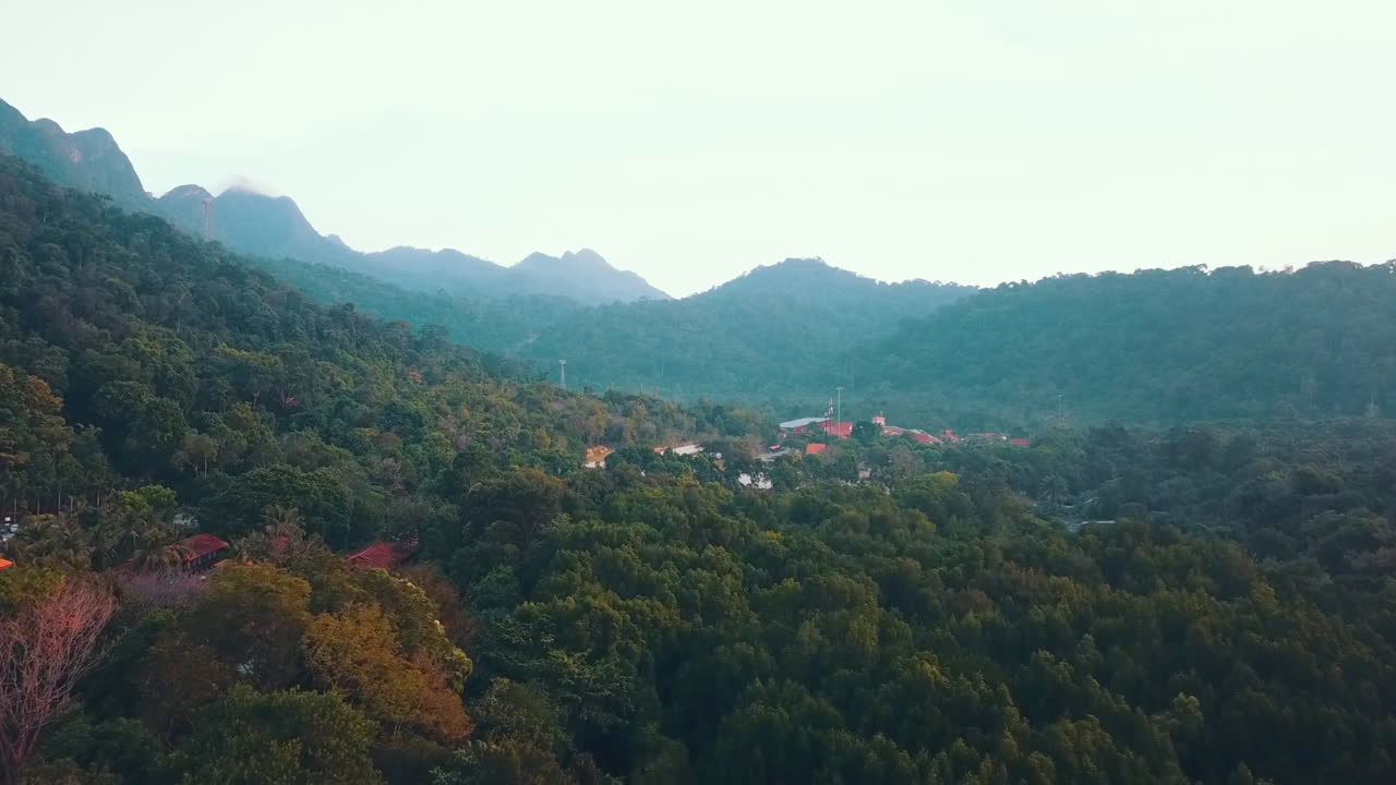 Tomada reveladora de uma vila no meio de uma floresta tropical com as montanhas ao fundo, Langkawi, Malásia.