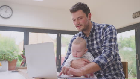 Berufstätiger-Vater-Benutzt-Laptop-Zu-Hause,-Während-Er-Sich-Um-Seinen-Kleinen-Sohn-Kümmert,-Der-Auf-Seinem-Knie-Sitzt-–-Aufnahme-In-Zeitlupe