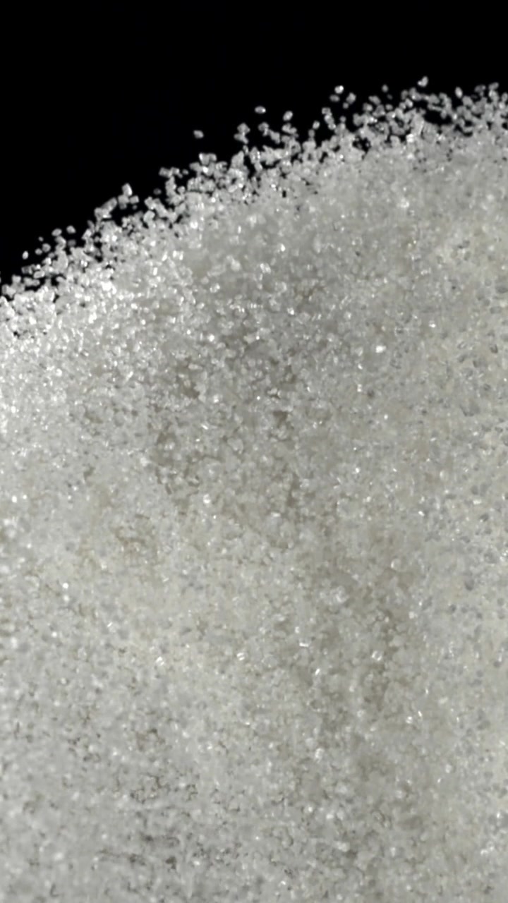 Granuli di zucchero bianco che si versano e si dissolvono su sfondo nero