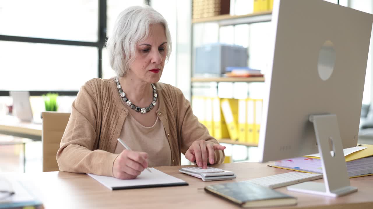 Donna anziana che calcola le finanze a una scrivania d'ufficio