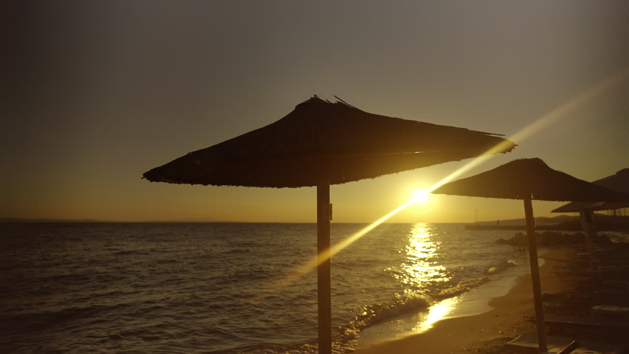 escena de la playa al atardecer con sombrillas de paja