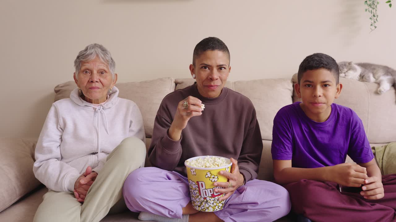 Famiglia multigenerazionale che guarda la TV e mangia popcorn sul divano