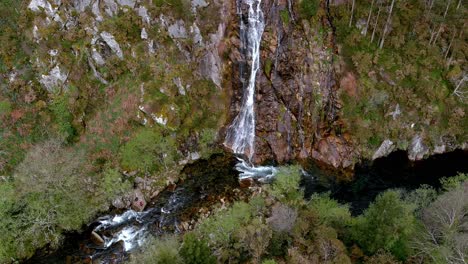 la cascada cae al río sor por el acantilado rodeada de bosques y gente tomando fotografías junto al río.