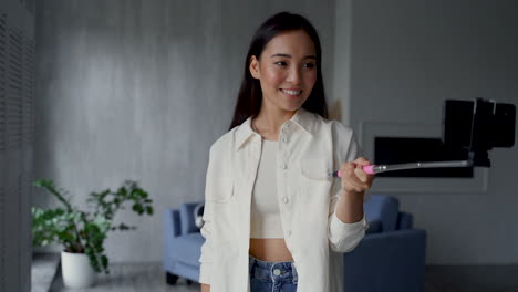 pretty young woman recording herself with a phone and a selfie stick, showing her home