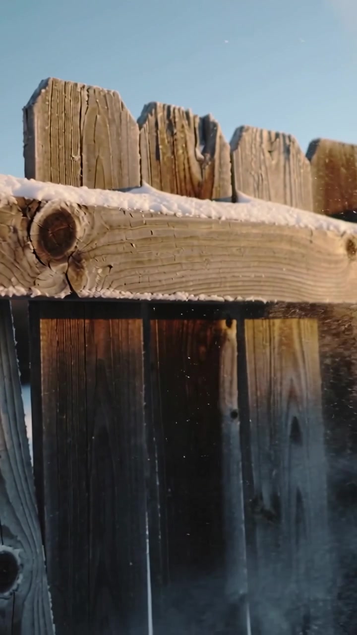 Video verticale: Un soffio che si alza sotto la ringhiera, creando una recinzione di legno che invia neve scintillante verso il sole nel cortile.