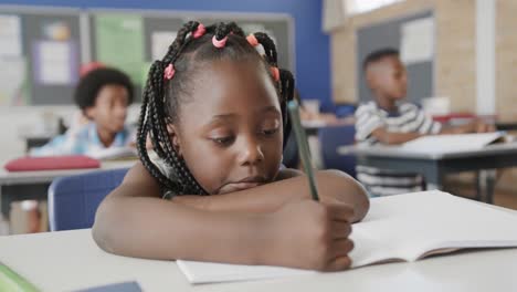 Retrato-De-Una-Feliz-Niña-Afroamericana-Escribiendo-En-El-Escritorio-En-Clase-De-Escuela-Primaria,-Cámara-Lenta