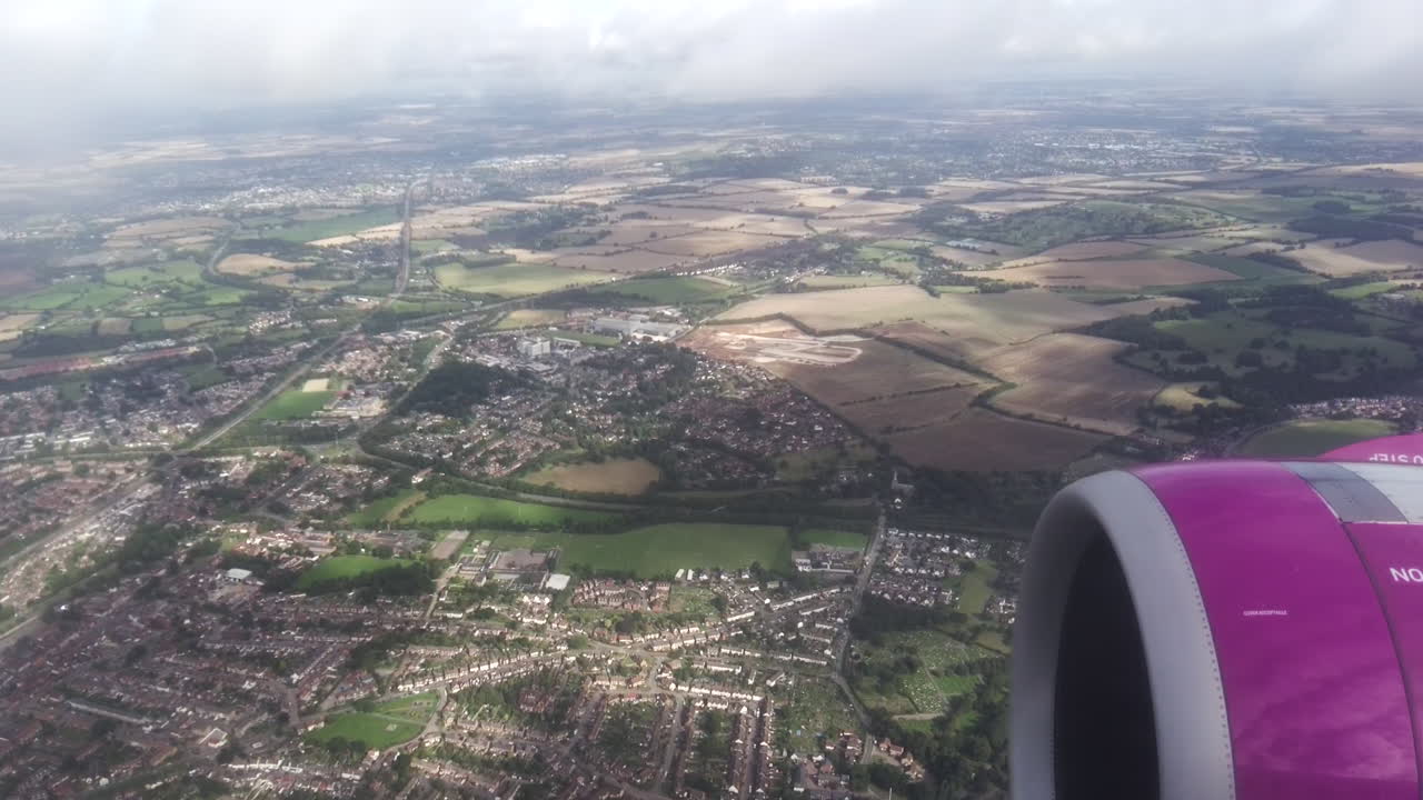 View of earth from a flying plane. Clouds, land with fields and town, plane engine