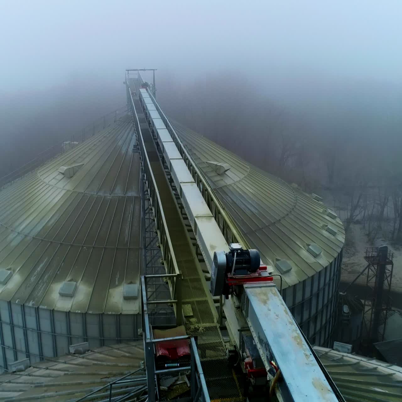 Dusty tops of the bin at grain elevator complex. Drone footage above the metal tanks at modern agricultural plant. Foggy weather backdrop