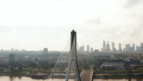 Fly-around-top-of-tall-bridge-pillar.-Revealing-cable-stayed-bridge-over-river-and-skyline-with-skyscrapers.-Warsaw,-Poland
