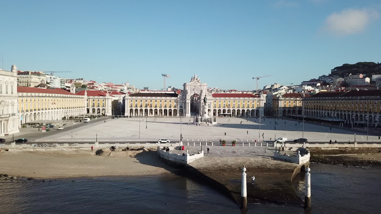 Lisbona, riprese con drone della Piazza del Commercio che si avvicinano dal fiume Tago, con le colonne del molo che passano attraverso la statua di Re José verso l'Arco della Rua Augusta in una giornata di sole con cieli azzurri.