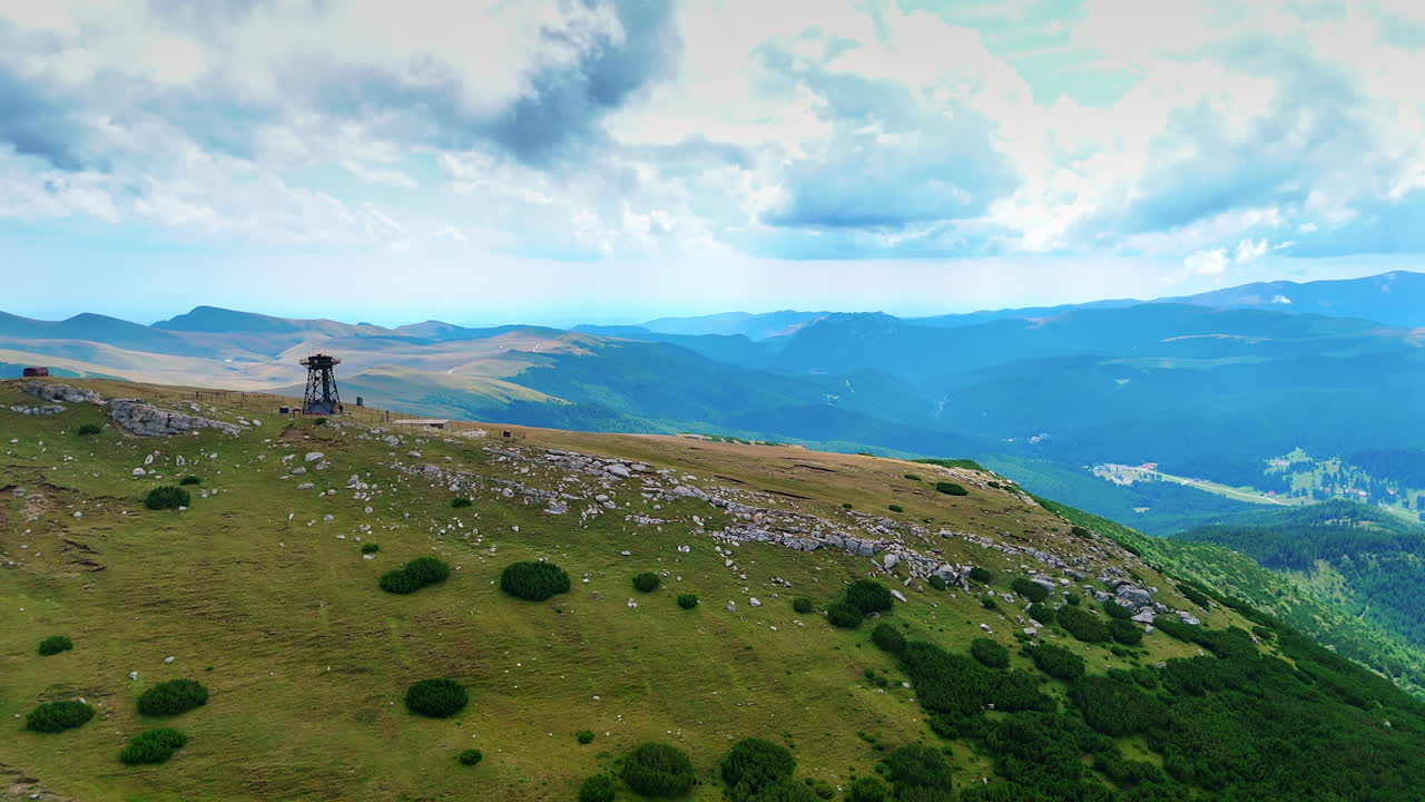 The scene shows a mountain landscape with grass and scattered rocks. There is a ski lift at the top surrounded by lush hills. Clouds cover parts of the sky