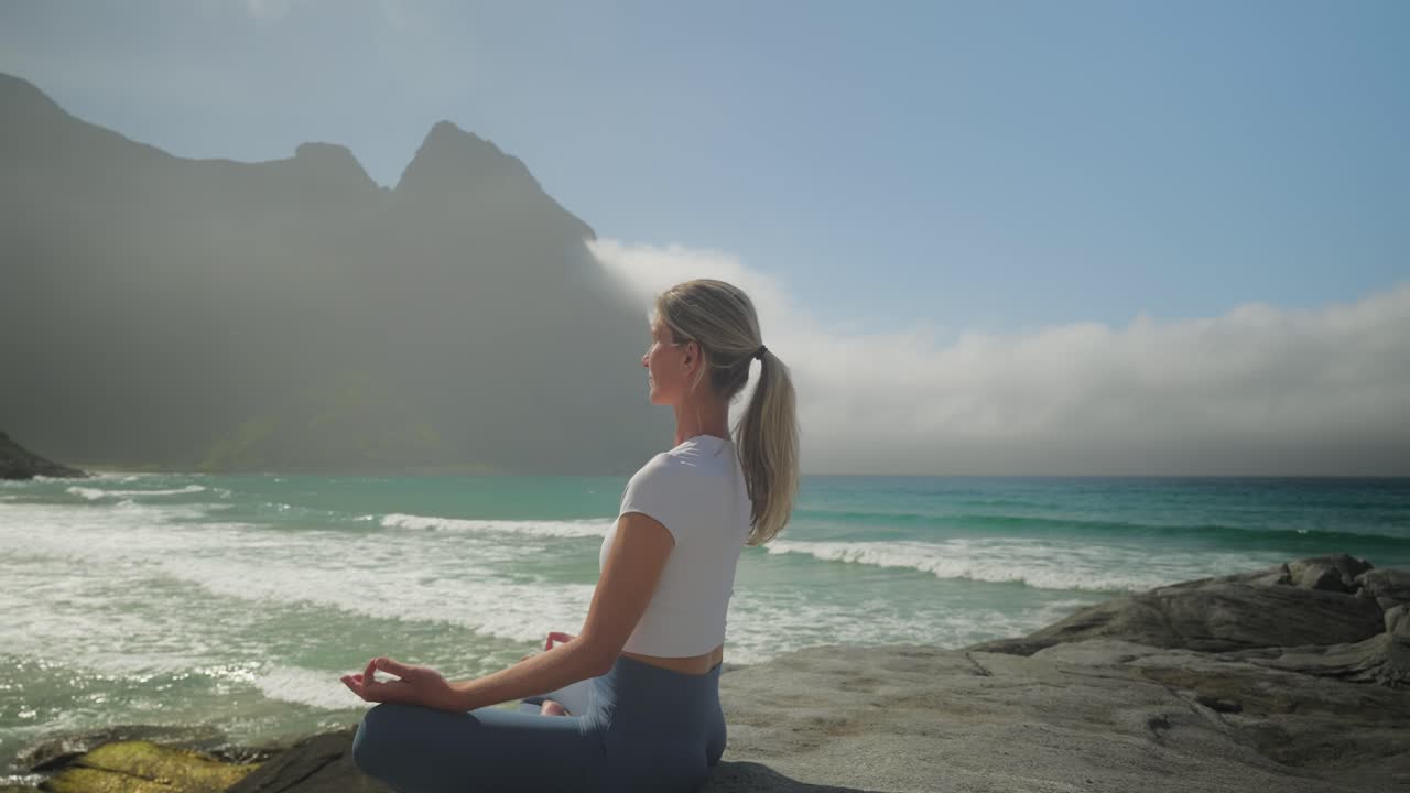 una mujer atractiva y sana medita en la playa de noruega, de cerca moviéndose hacia atrás.