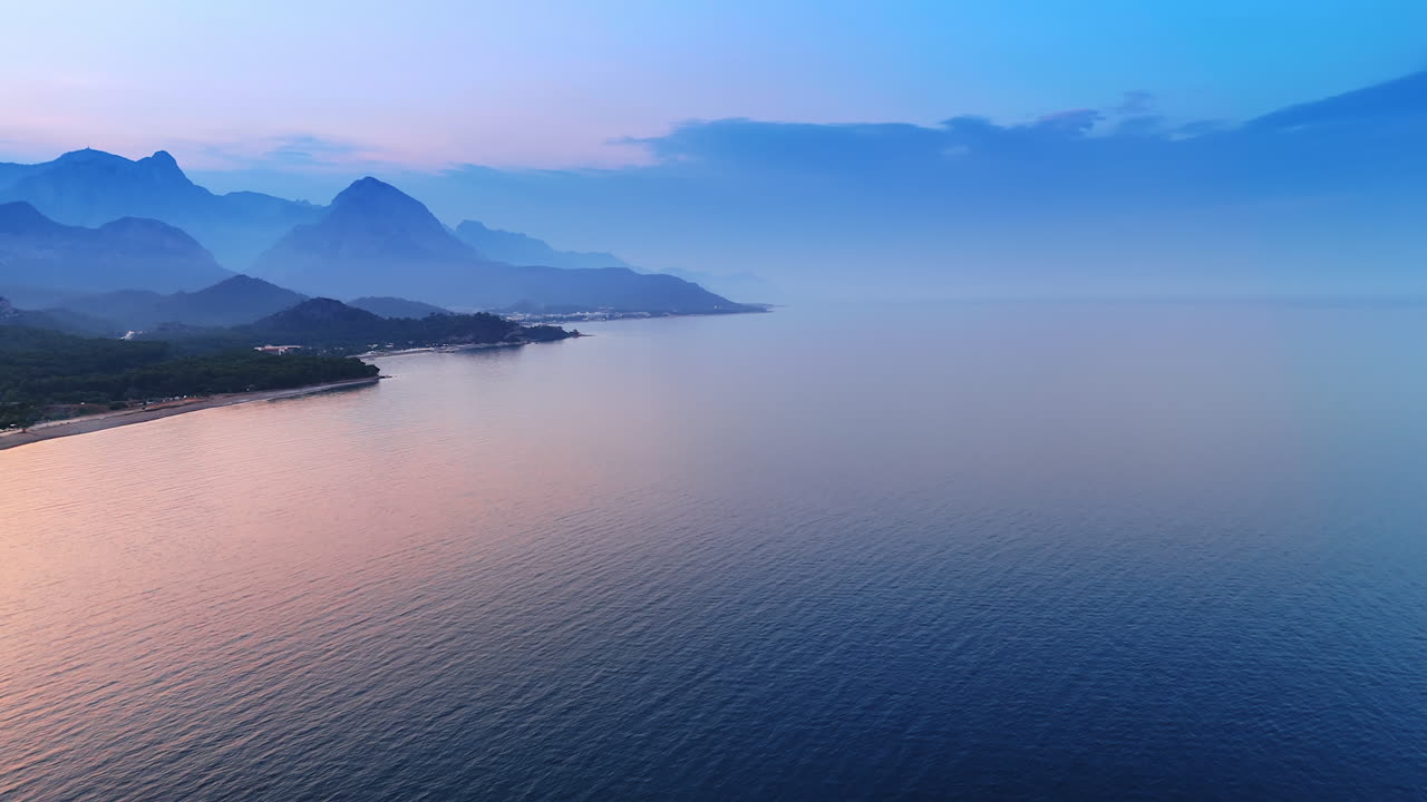 Idyllic view of the beautiful calm waterscape colored pink at dusk time. Mountain silhouettes on the shore. Aerial perspective