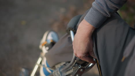 close up of person in gray clothing adjusting black and orange strap on stilt, hands working with focus and precision, outdoor background blurred, emphasizing action of securing and fixing equipment