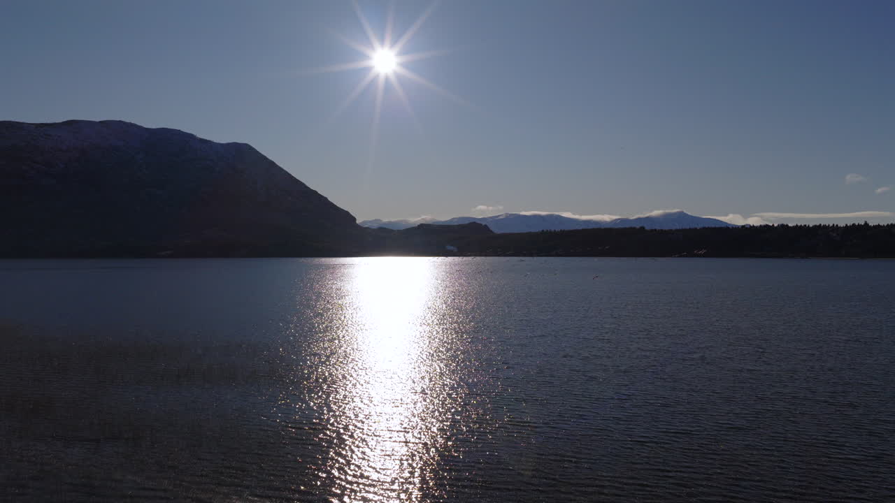 Sun reflecting on highland lake surface in aerial view at sunset with mountain silhouettes in Patagonia, Argentina
