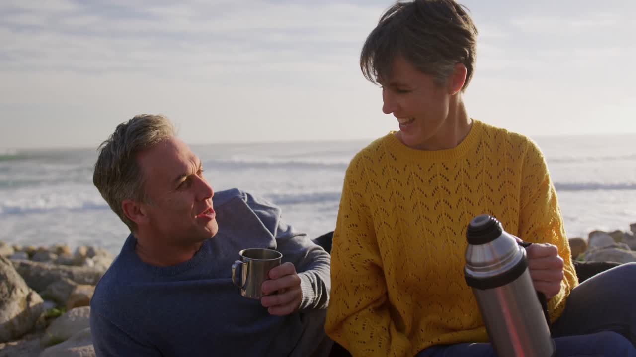 Par drikker kaffe ved havet.