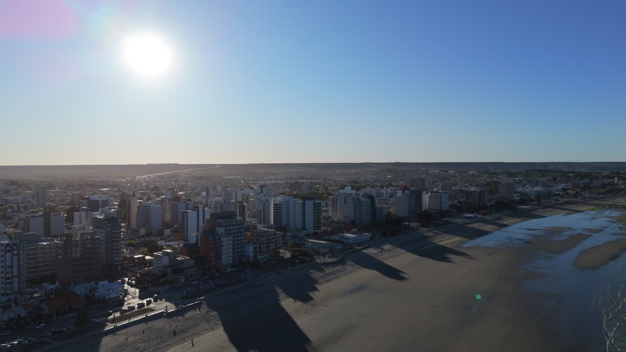 Beautiful sunny cityscape of Puerto Madryn, big beach with waves on the water, blue sky aerial view, copy space, dolly shot backwards