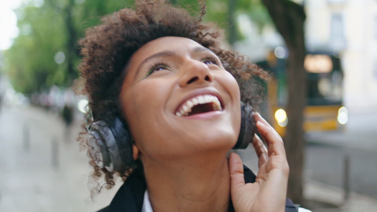 Woman wearing headphones dancing along on city street closeup. Girl in headset