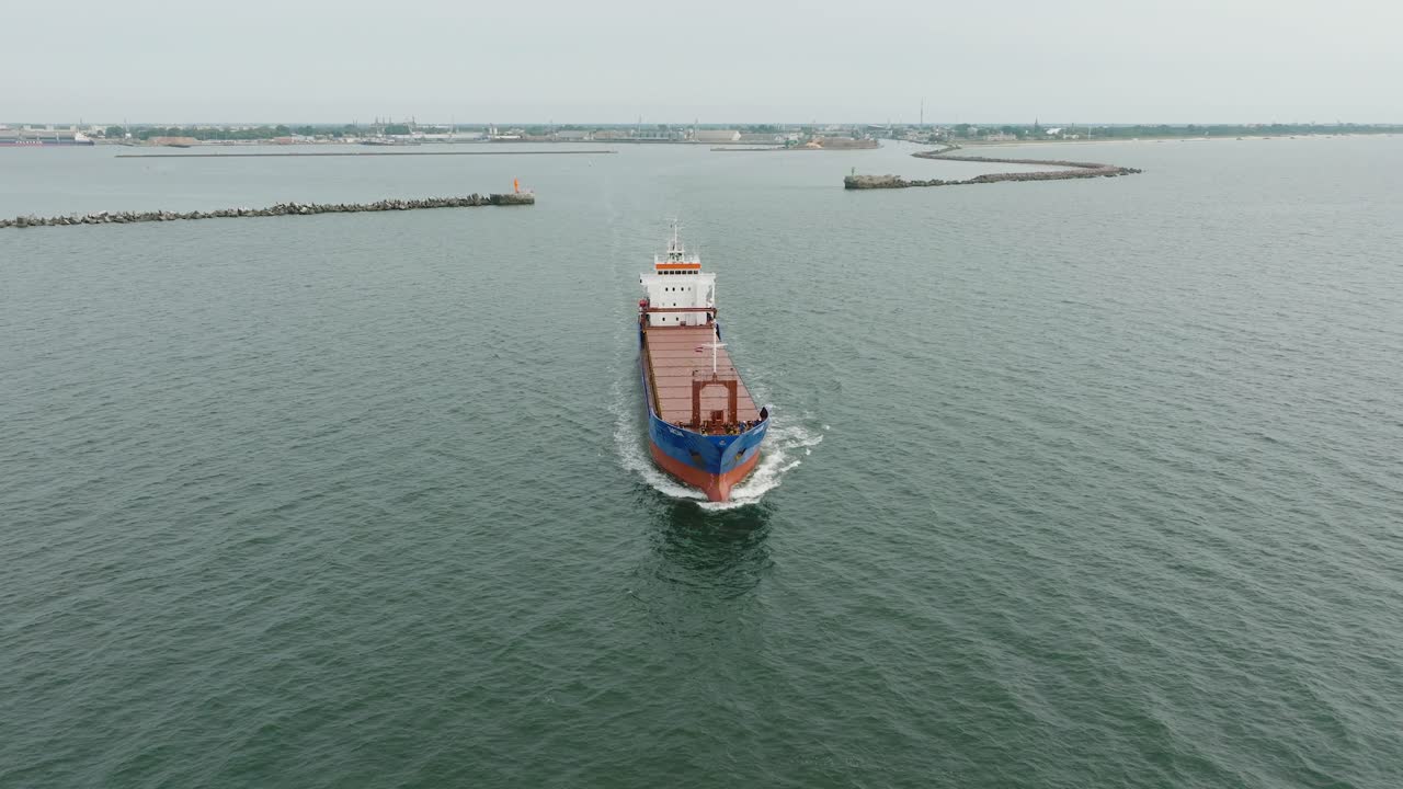 vista aérea del gran buque de carga azul que sale del puerto de liepaja, puente de karosta, día ligeramente nublado, mar báltico tranquilo, tiro de avión no tripulado que se mueve hacia atrás