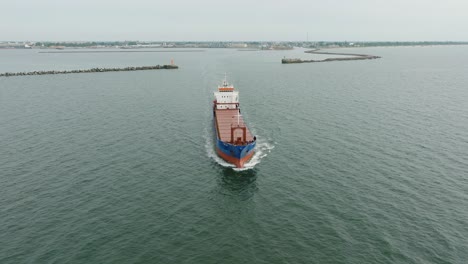 aerial establishing view of large blue cargo ship leaving port of liepaja , karosta bridge, slight overcast day, calm baltic sea, wide drone shot moving backward