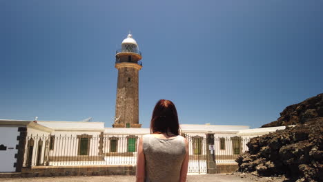 woman with her back turned, admires the orchilla lighthouse on the island of el hierro on a sunny day