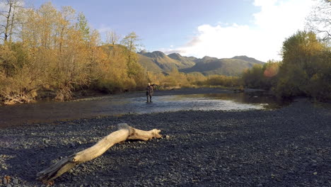 A-nature-and-wildlife-photographer-walks-across-a-salmon-river-after-finishing-a-fall-photoshoot-in-the-wilderness-of-Kodiak-Island-Alaska