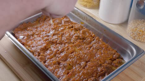 medium shot of adding bechamel sauce to tomato sauce in a baking tray for making lasagne