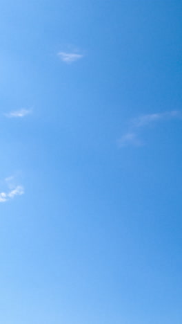blue sunny sky clears up from white clouds. light spindrift clouds flying quickly by the horizon disappearing from sight. vertical video