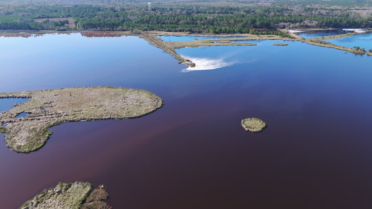 imágenes aéreas de una gran masa de agua que es azul y rodeada de bosque, al lado de una planta de papel industrial
