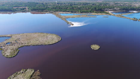 Aerial-footage-of-a-large-body-of-water-that-is-blue-and-surrounded-by-forest,-next-to-a-industrial-paper-plant