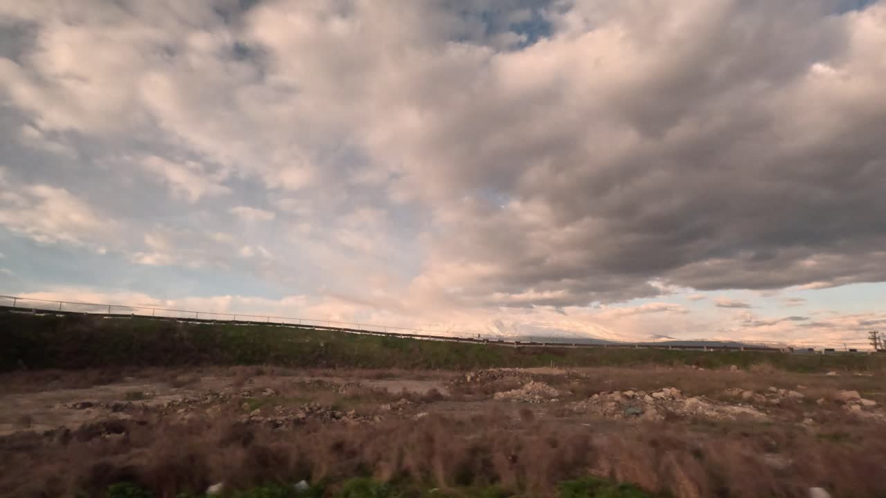 Himlen viser skyer over landskabet med bjerge i baggrunden i den tidlige aften. Området er roligt med få synlige strukturer og naturlige omgivelser.