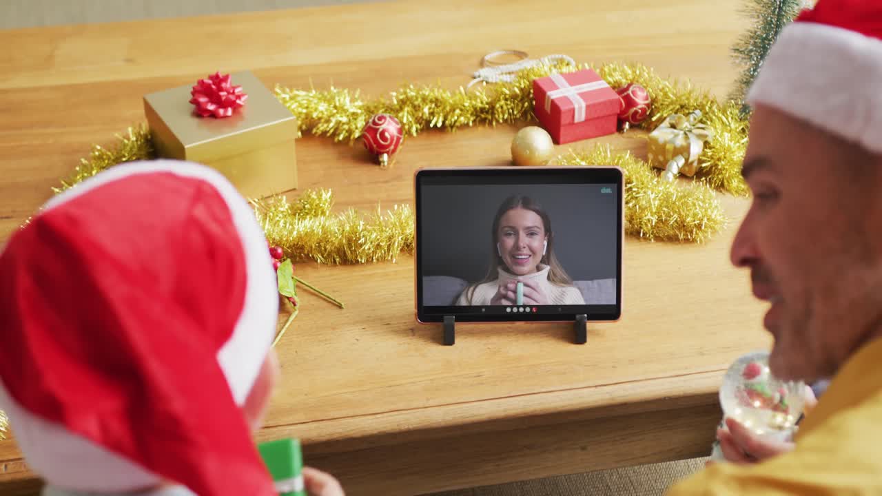 padre y hijo caucásicos con sombreros de santa usando una tableta para una videollamada de navidad con una mujer en la pantalla