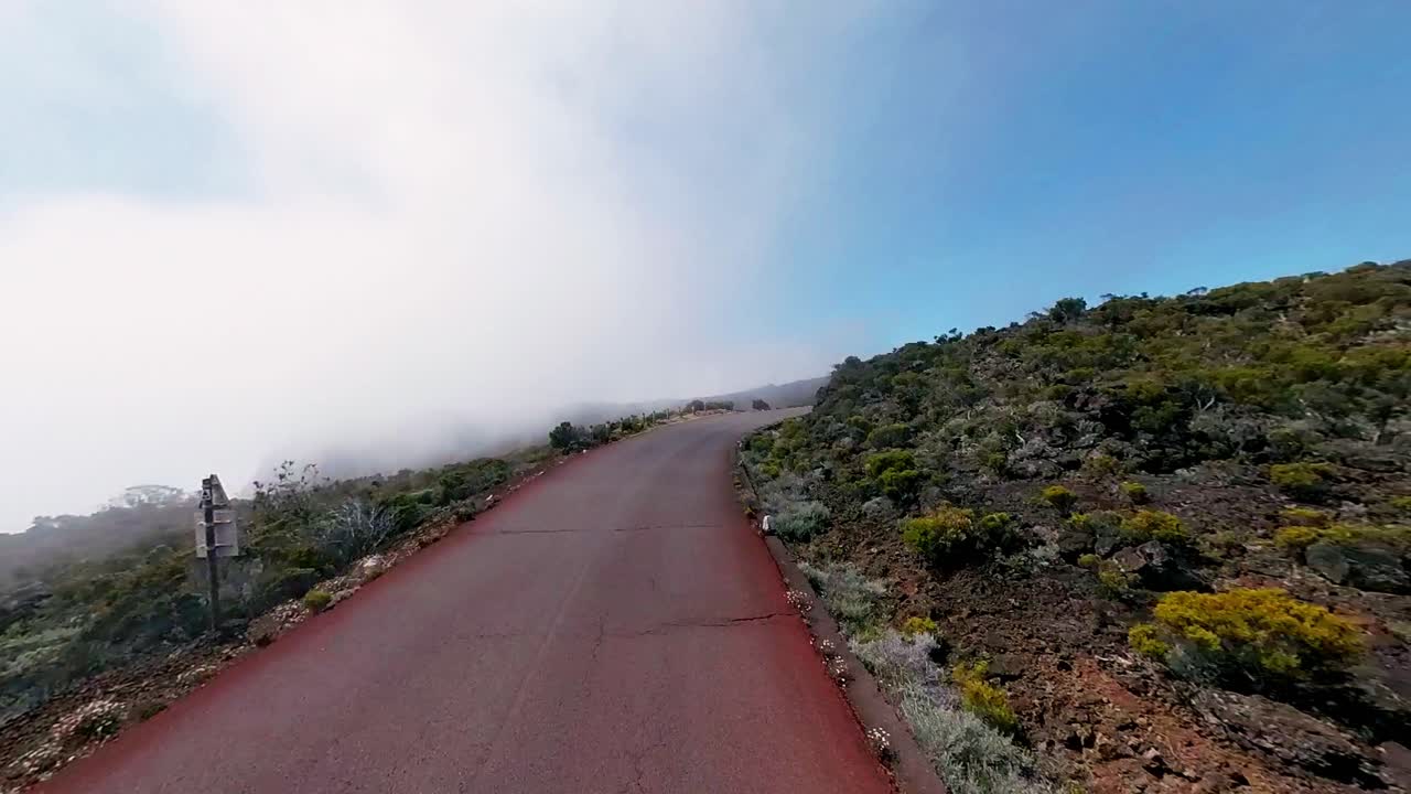 Atmospheric drone footage capturing a car winding through misty mountain roads in Reunion Island. Dramatic fog creates mystical scenery in this French territory.