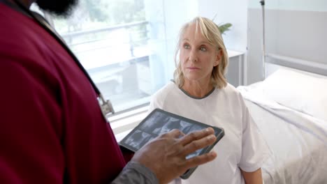 african american male doctor with digital tablet talking to caucasian female patient at hospital