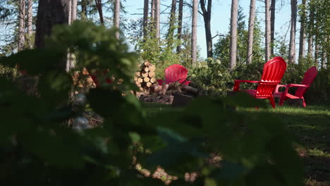 A-bonfire-with-four-plastic-chairs-around-it-is-revealed-behind-the-bushes-in-the-forest-on-a-sunny-day