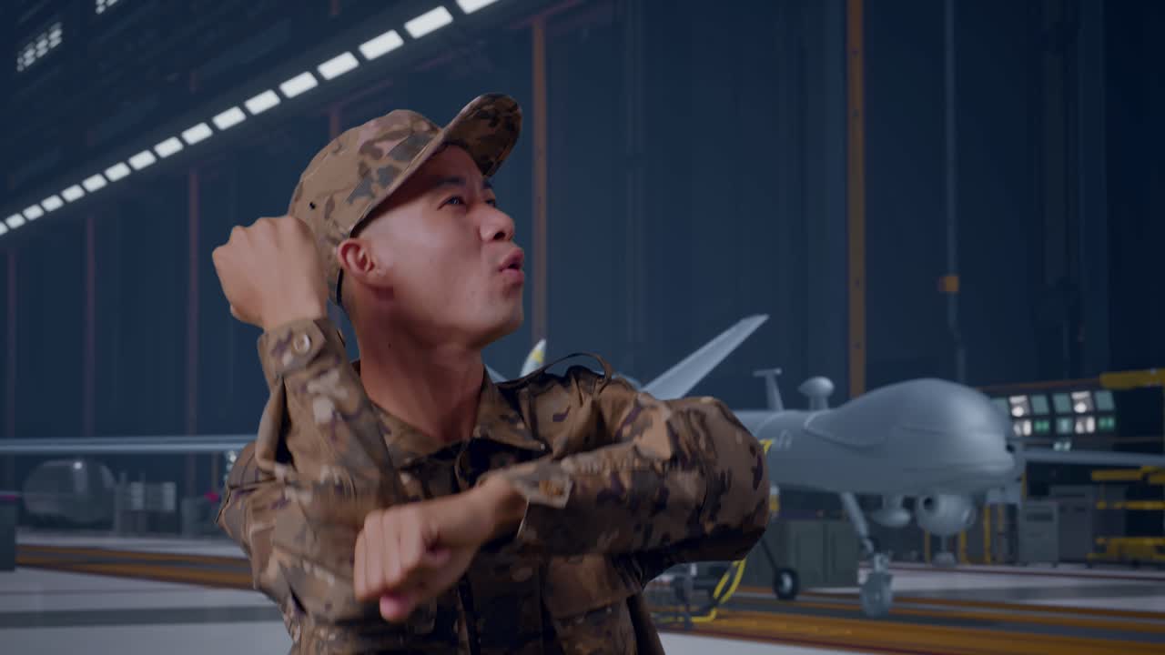 Primo piano di soldato asiatico che balla mentre è in piedi con un moderno drone militare in un hangar di manutenzione.