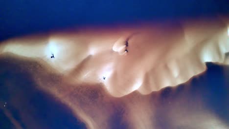 aerial view of sand dunes and dark water, camera pans left, dark water and light sand dunes create texture, birds in flight visible