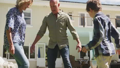 Happy-senior-caucasian-couple-with-grandson-playing-football-in-garden