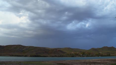 The-mesmerizing-time-lapse-transformation-of-a-summer-storm,-as-gusts-of-wind-whip-up-swirling-dust-along-the-river,-creating-a-captivating-display-of-nature's-power-and-beauty