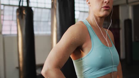 retrato de una mujer caucásica en forma con auriculares con las manos en las caderas de pie en el gimnasio